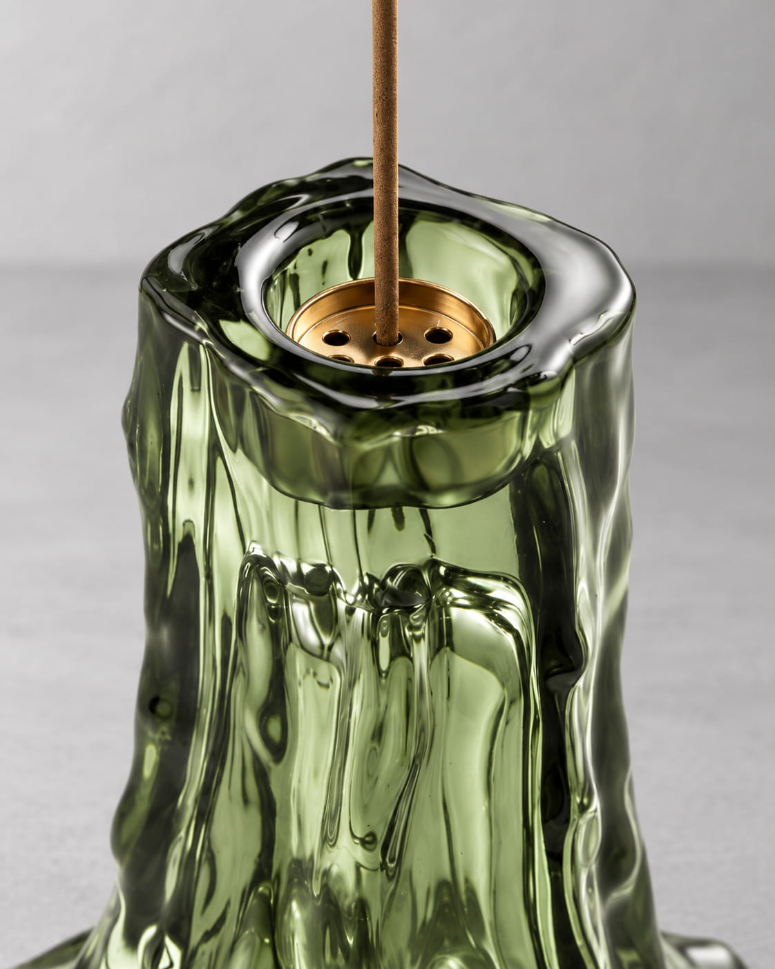 Close-up of a moss green glass incense holder showing the metal insert and molten glass texture