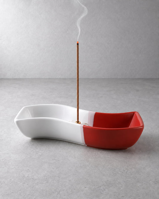 Red and white ceramic incense holder for sticks with burning incense and soft rising smoke.