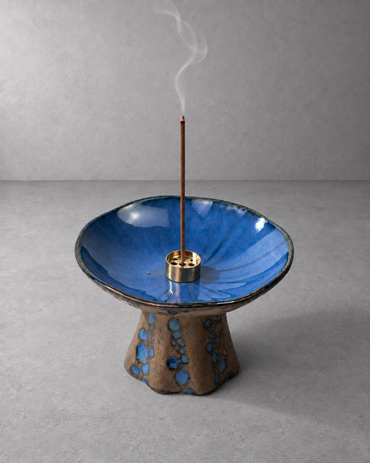 Blue ceramic incense holder for sticks with reactive glaze, burning incense, and soft rising smoke.