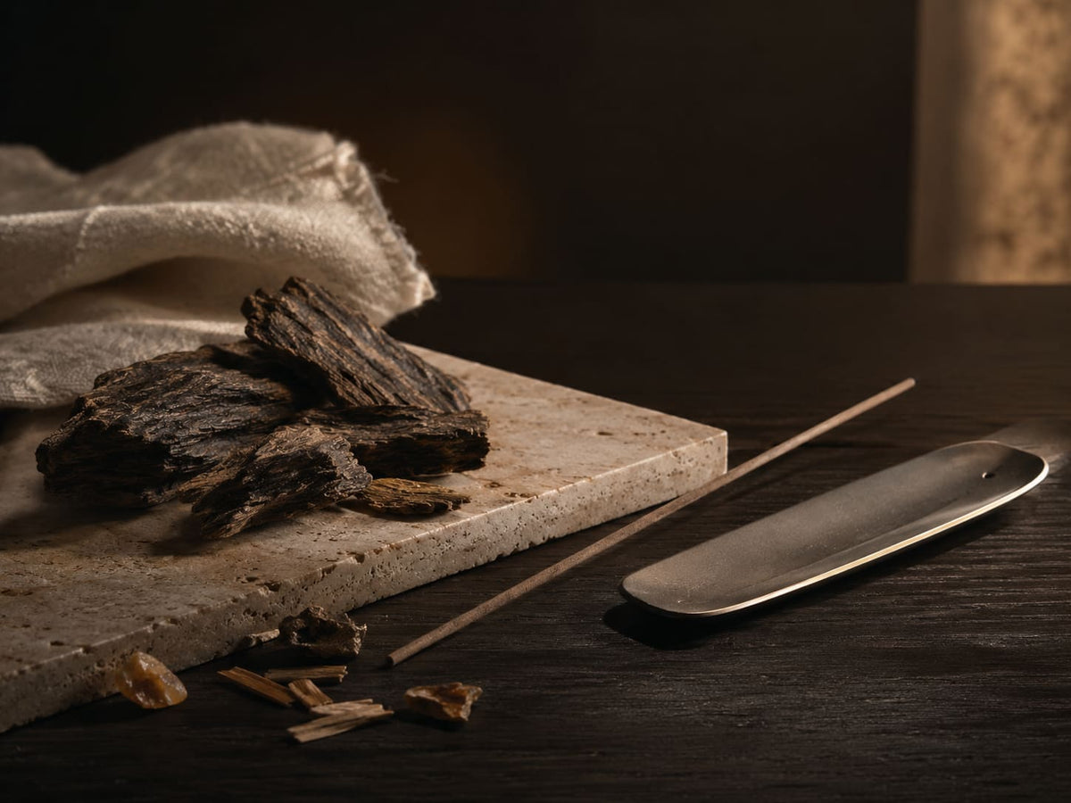 Fragrant wood pieces, incense stick, and sculptural incense holder arranged in a dark VELORIEN material study.