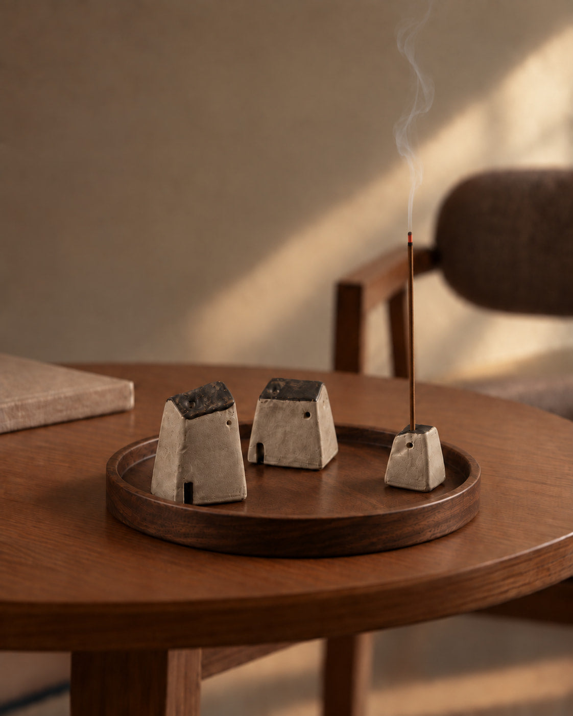Homeward Ceramic Incense Holder Set displayed on books in a moody interior scene, with one holder burning incense and soft smoke rising.