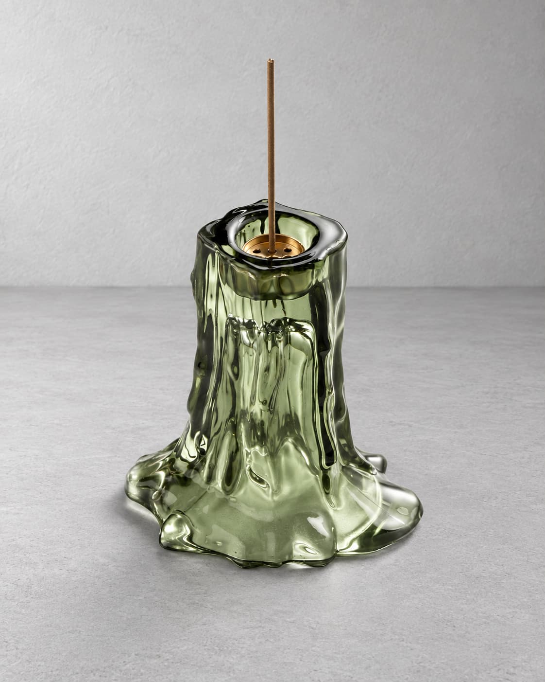 Moss green melted glass incense holder with a single incense stick on a light gray background