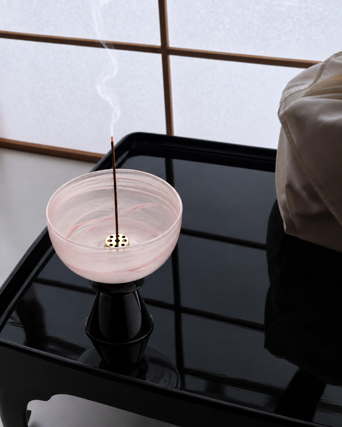 Rosé Cloud Glass Incense Holder with softly clouded pink glass and black pedestal base, styled on a glossy black table beside a softly lit window.