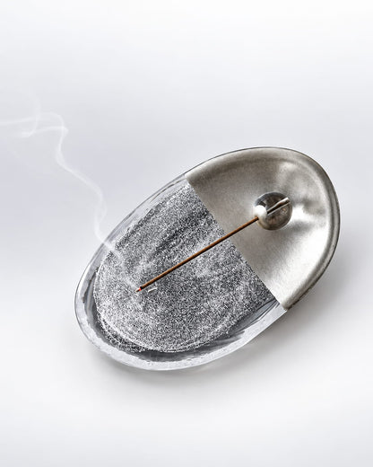 Silver and clear glass incense holder for sticks with burning incense and soft rising smoke.