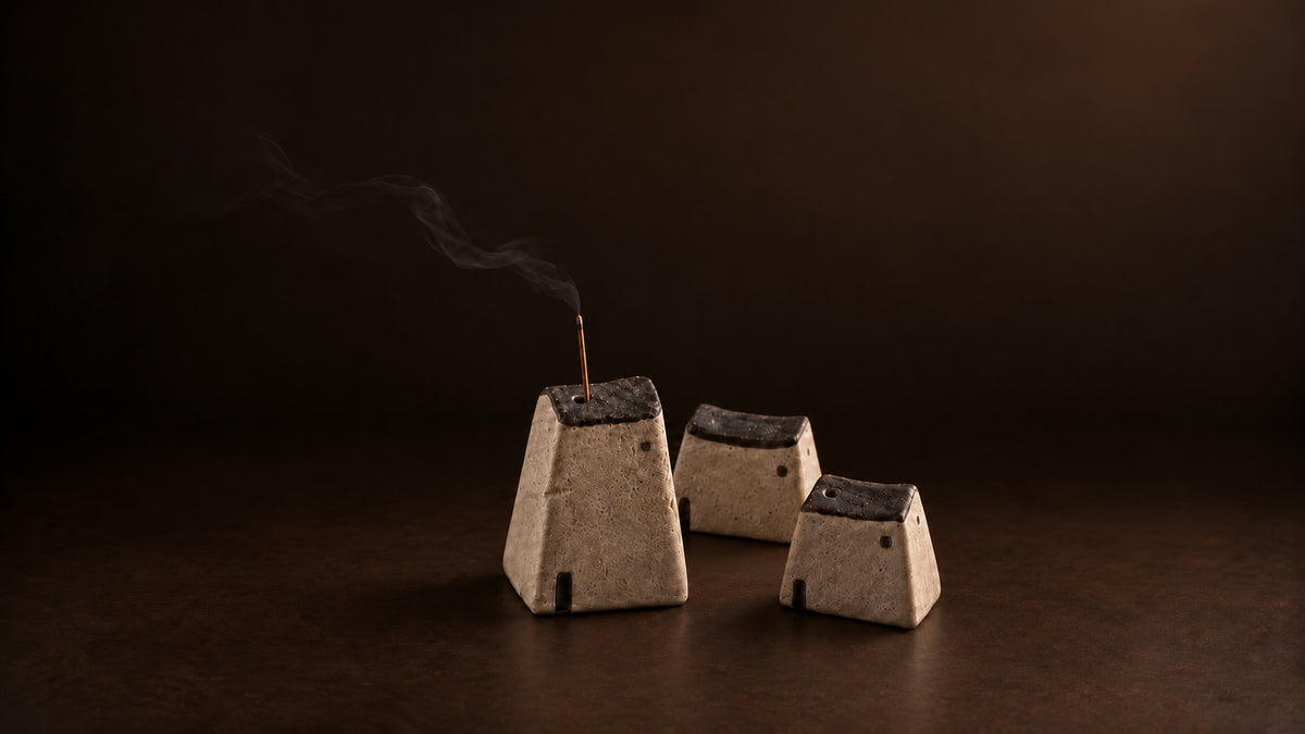 Three sculptural ceramic incense holders with a burning agarwood incense stick in a dark minimalist ritual setting.