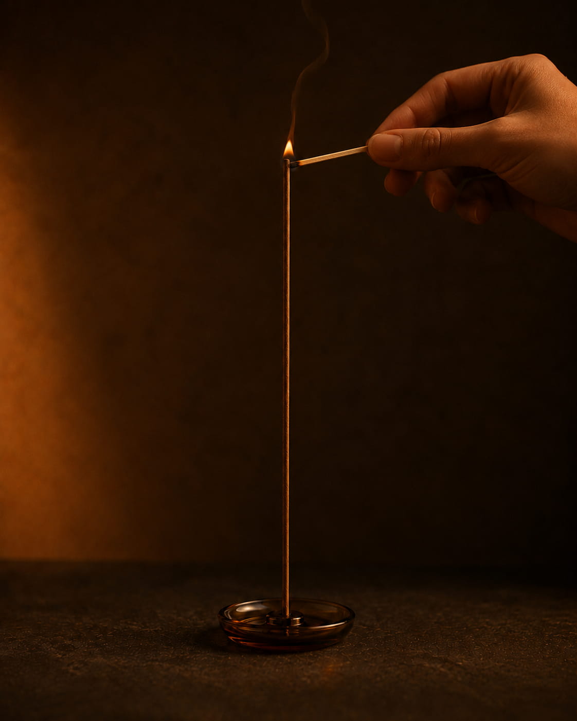 Hand lighting the tip of an agarwood incense stick with a burning match