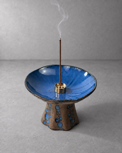 Blue ceramic incense holder for sticks with reactive glaze, burning incense, and soft rising smoke.