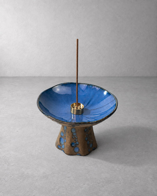 Azure blue reactive glaze ceramic incense holder with an unlit incense stick, raised pedestal, and gold-tone center insert.