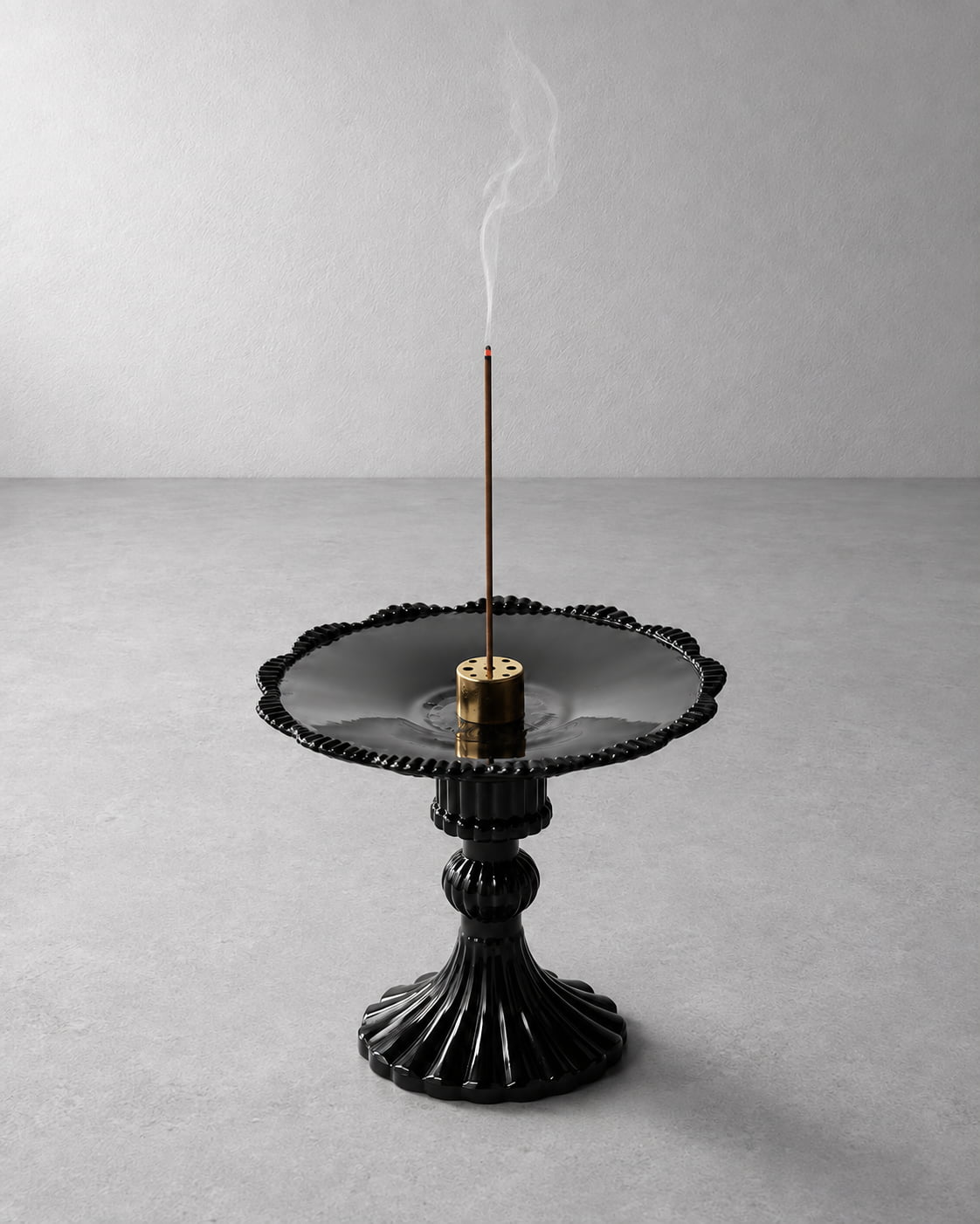 A black ceramic incense burner with a fluted pedestal base and scalloped rim, holding a smoking incense stick on a light gray background.